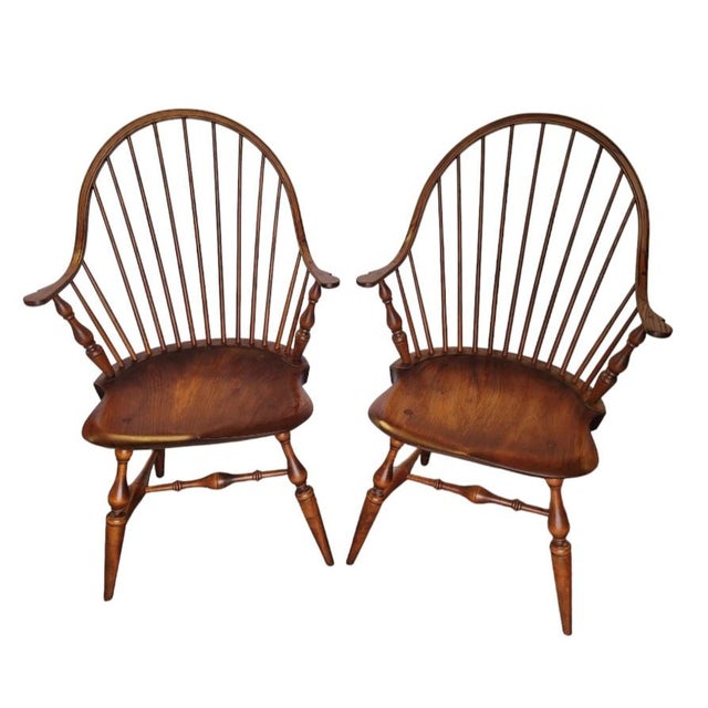 A fine pair of bow back windsor armchairs featuring elm wood construction, continuously curved arms, spindle backs turned...