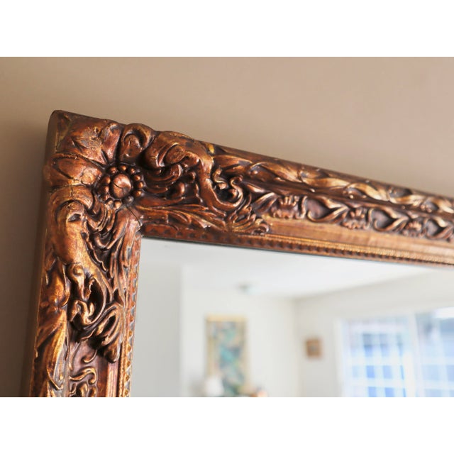 Vintage carved wood mirror finished in hand-painted gold gilt. Carved design features florals and beaded studs framing the...