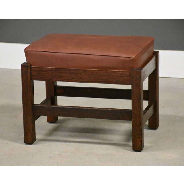 An arts and crafts oak footstool by L. & J.G. Stickley with a leather cushion ready to be place in front of a lounge...