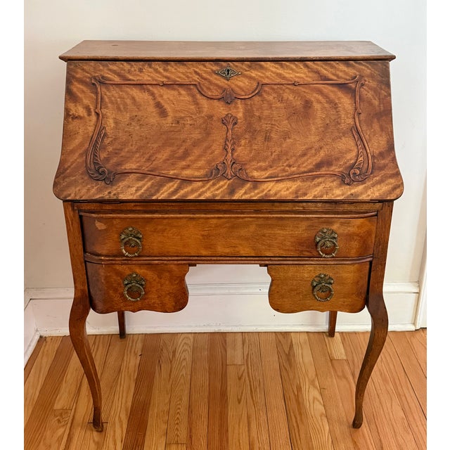 An antique French Provincial tiger maple slant-front secretary desk with applied cartouche molding, brass ring pulls,...