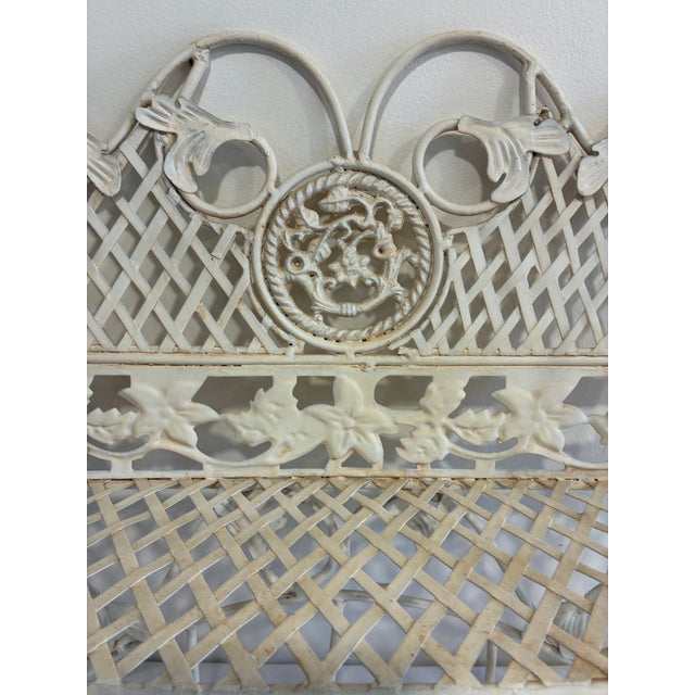 A charming white painted wrought iron wall shelf featuring intricate lattice-work paneling, scrolling floral vine...