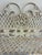 A charming white painted wrought iron wall shelf featuring intricate lattice-work paneling, scrolling floral vine...
