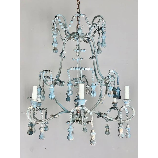 Hand crafted wood & metal painted 6-light chandelier with wood beads and unique carved tassels hanging throughout. The...