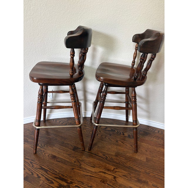 A handsome matched pair of vintage Ethan Allen Old Tavern swivel bar stools, model 12-9505, combining classic Early...
