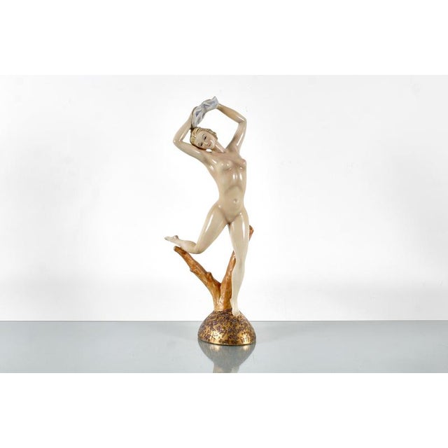 Delightful hand-painted ceramic sculpture depicting a naked girl on a golden base, resting on a tree trunk. Italian...