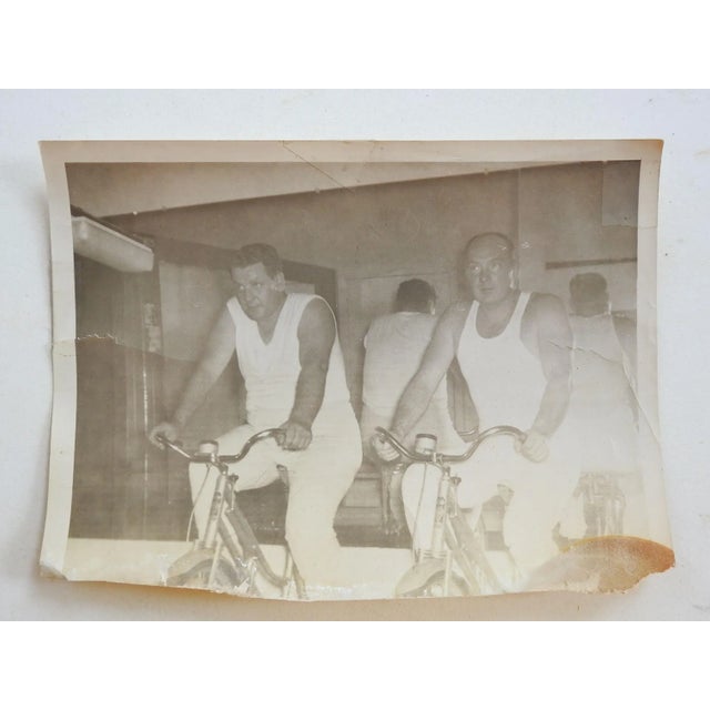 Circa 1950's photograph of 2 men on stationary bicyles. Working out in front of mirror in sleeveless white tees and...
