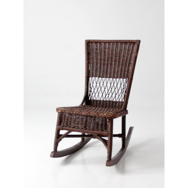 Early 20th century Victorian wicker rocking chair featuring a tall woven back, open lattice detailing, and a rich dark...