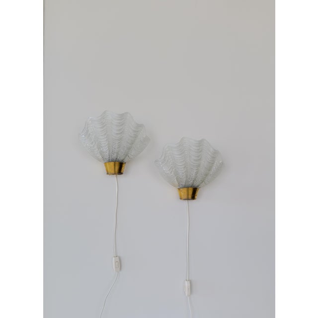 This pair of wall lights in brass and glass were produced by ASEA, Sweden, 1950s. The glass made to look like seashells is...