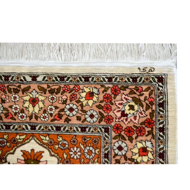A brilliant vintage silk Turkish Hereke rug woven with a central medallion with a mirrored floral pattern woven in pink,...
