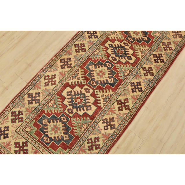 A tribal Caucasian Kazak runner hand-knotted with fine wool on a cotton foundation. This rug features geometric medallions...
