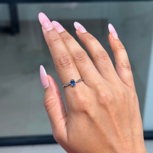 This minimalist solitaire ring features a 0.64 carat natural oval blue sapphire, set in 14k white gold. The Blue Sapphire...