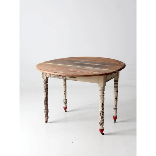 This is an antique drop leaf table. The farmhouse table features turned legs on casters. Aged white and red paint with...