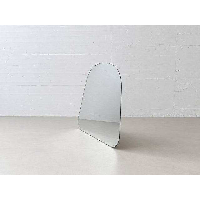 A distinctive, freestanding mirror with a softly rounded, asymmetrical shape and a minimalist design. The frameless mirror...