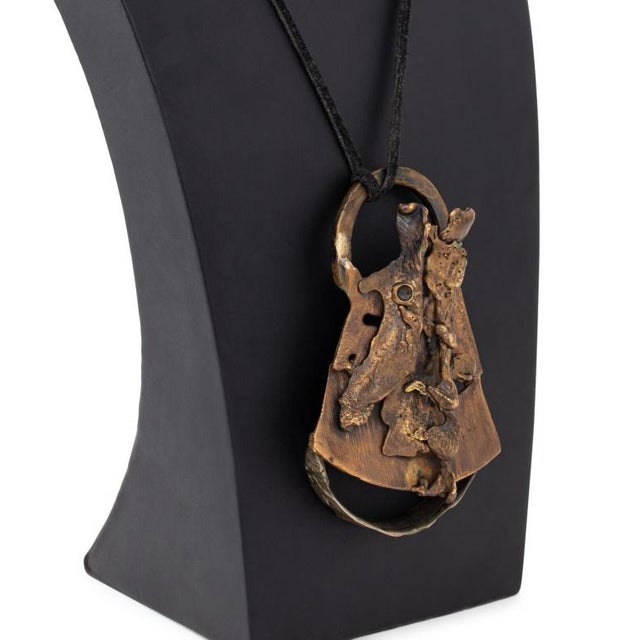 Brutalist Studio Jewelry Necklace, featuring abstract shape attached to triangular base, hung on black cord, apparently...