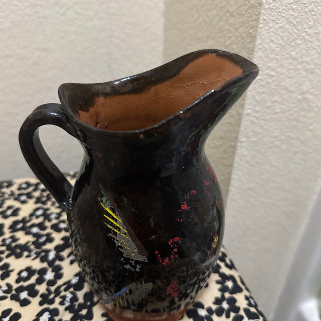 Decorative stoneware pitcher finished in a deep, dark glaze and accented with a distinctive yellow and red line motif. The...