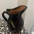 Decorative stoneware pitcher finished in a deep, dark glaze and accented with a distinctive yellow and red line motif. The...