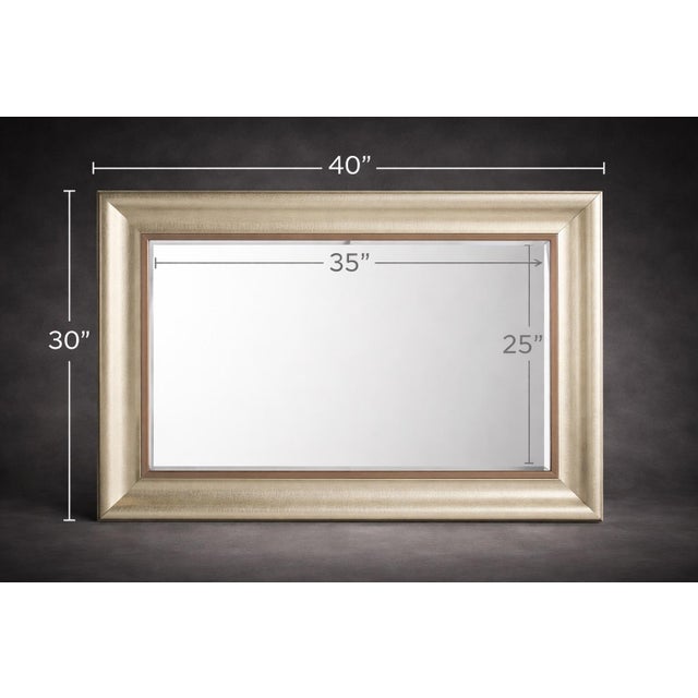A large, statement-scale rectangular wall mirror with a warm champagne-silver frame and copper-toned inner liner, offering...