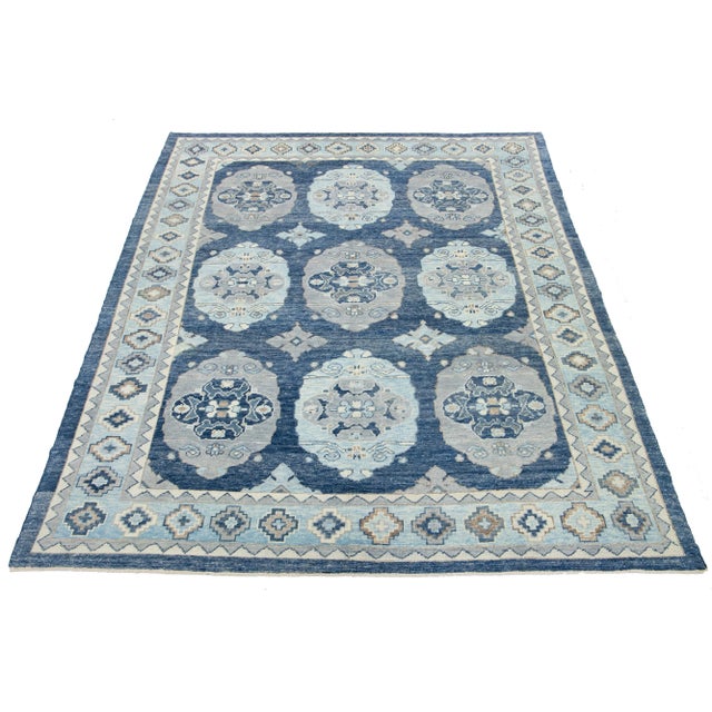 This stunning hand-knotted wool rug features a bold blue base with a captivating gray and ivory pattern, making it the...