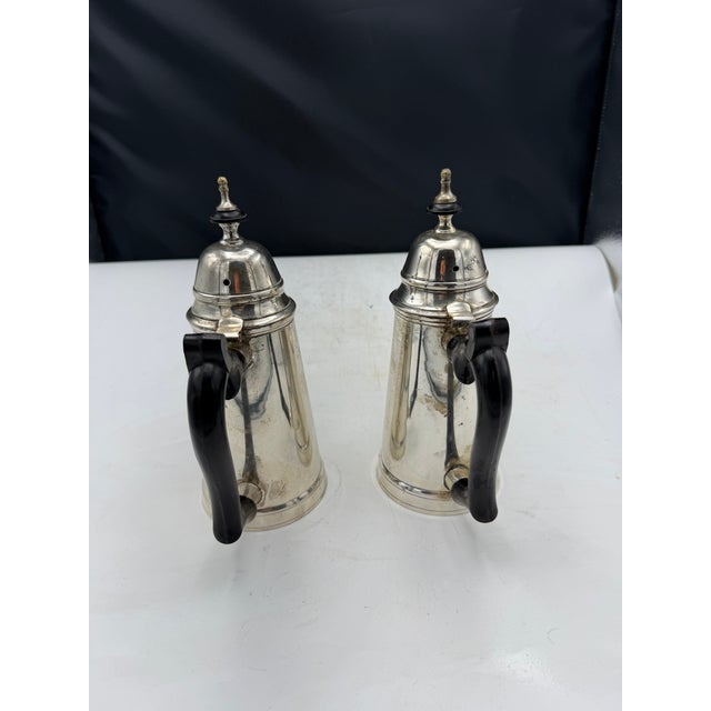 Matching silverplate coffee pots with hinged lids and black handles. The set includes one pot with a spout and one...