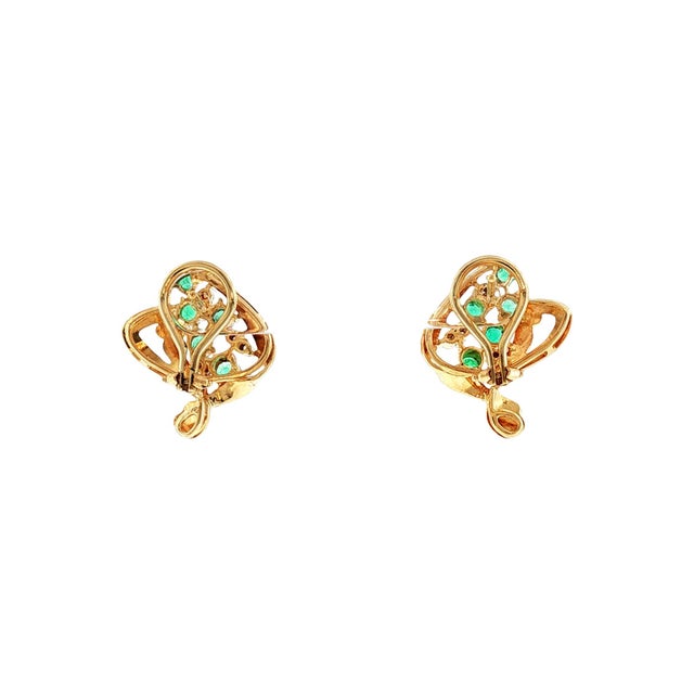 A pair of 1960s 18k gold earrings featuring round green emeralds and brilliant white diamonds. The emeralds have an...