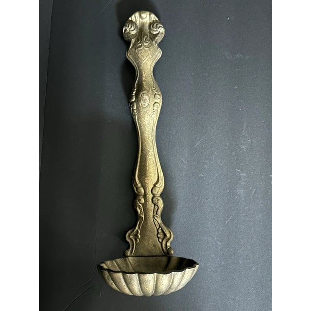 Vintage mid 1900s decorative wall hanging ladle spoon. It is a gold in color with ornate detailing and a scalloped shell...