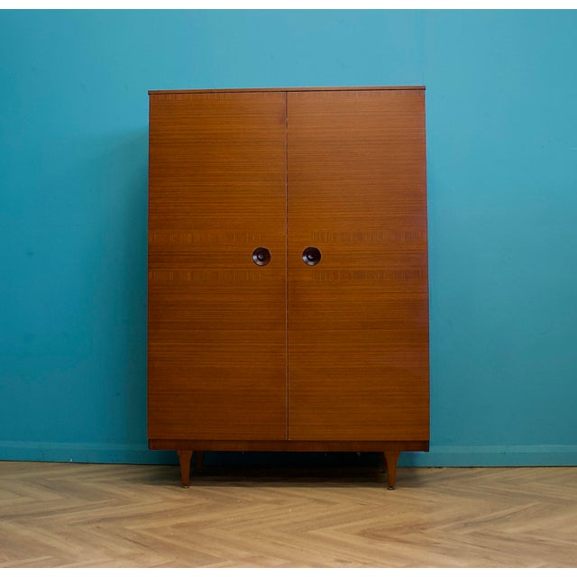 A mid-century Stonehill teak double wardrobe raised on tapering legs, featuring original ebonised recessed circular...