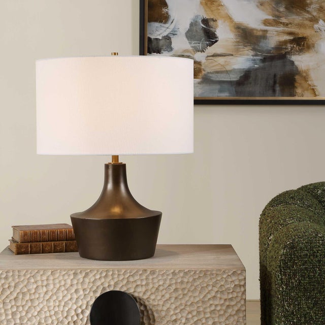This Striking Table Lamp Features A Gracefully Curved Base In A Warm Bronze Finish, Accented By Plated Antique Brass...