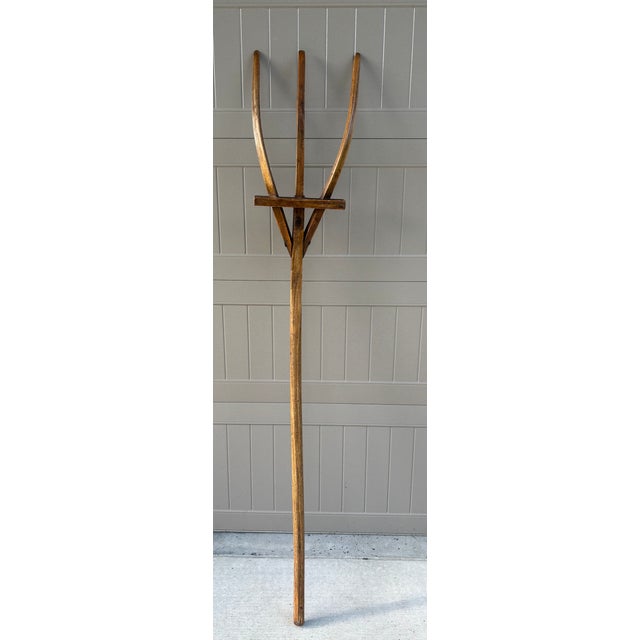 This antique American wooden hay fork features three elegantly arched tines rising from a long, hand-hewn shaft....