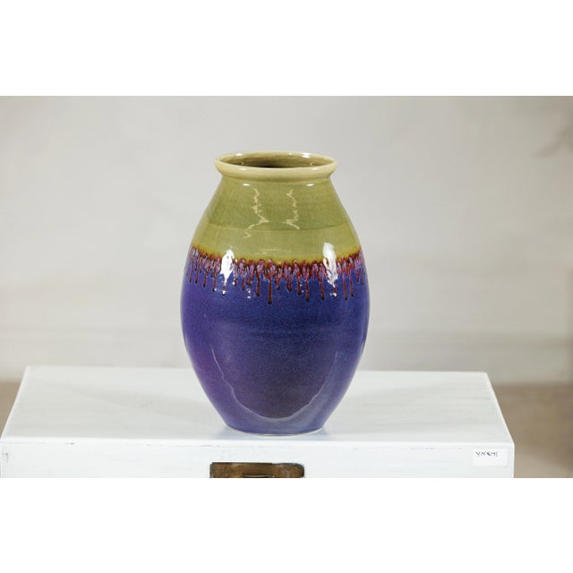 This richly glazed ceramic vase displays a striking contrast of colors and textures, with a bold palette that moves from...