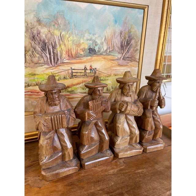 A cohesive set of four hand-carved wooden figurines depicting seated folk musicians, each holding a different instrument....