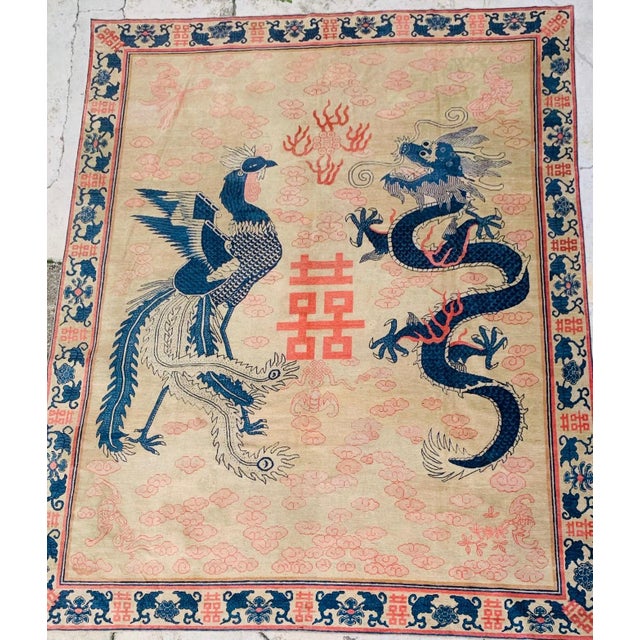 An impressive antique Chinese wedding carpet featuring a dramatic dragon and phoenix composition surrounding the prominent...