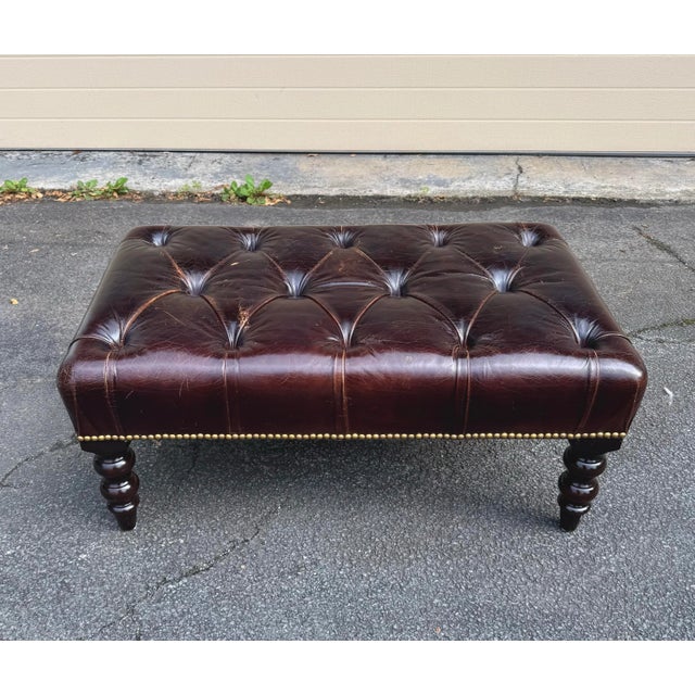 George Smith ottoman in dark brown tufted leather with mahogany wood turned legs.