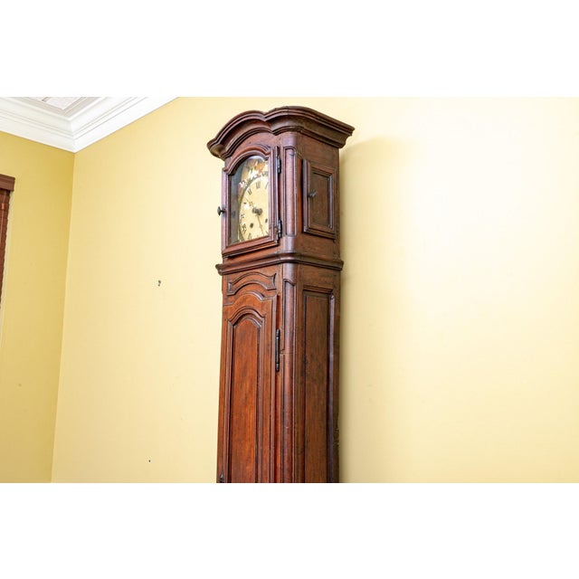 A towering 19th Century French walnut tall case clock with a graceful arched top, wooden hand-painted clock face with a...