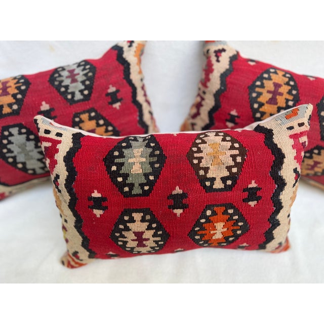 A set of three pillows upholstered in richly textured kilim weave, featuring warm red tones and distinctive hexagonal...