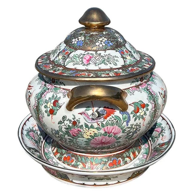 A large oval chinoiserie ceramic tureen with lid and underplate. This ceramic dish is hand-painted and decorated with a...