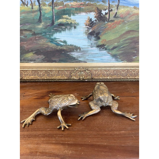 This pair of vintage brass toned frog sculptures features a charming and lifelike representation of crouching frogs,...