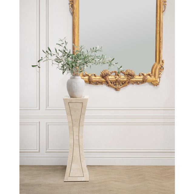 A sculptural hourglass-form pedestal stand painstakingly crafted out of tessellated stone with an elegant inset brass trim...