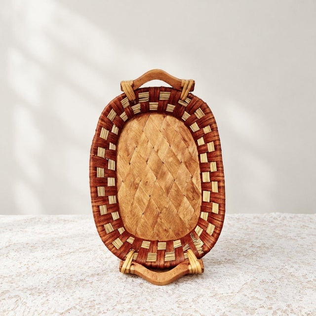 This oval-shaped tray is hand-woven from natural rattan. The edge of the tray is interlaced with two-color rattan to form...