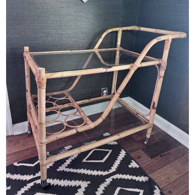 This 1960’s rattan bar cart is great as a table, party zone or accent piece, with two glass shelves on brass and rubber...