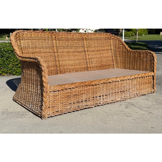 A striking vintage woven rattan lounge sofa featuring a dramatic curved silhouette and oversized braided trim. Its...