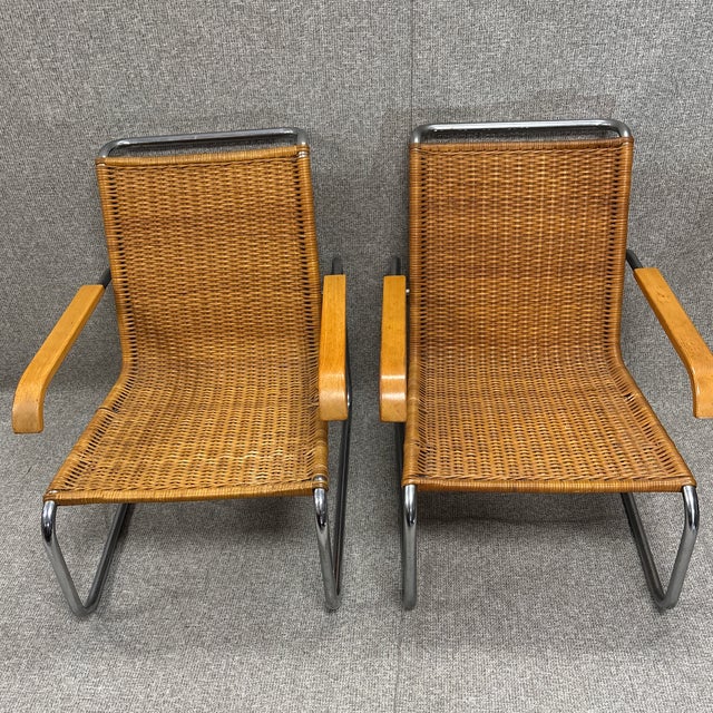 Pair of Chairs in the Manner of Marcel Breuer. Featuring a steel frame and woven wicker armchairs, these chairs combine...