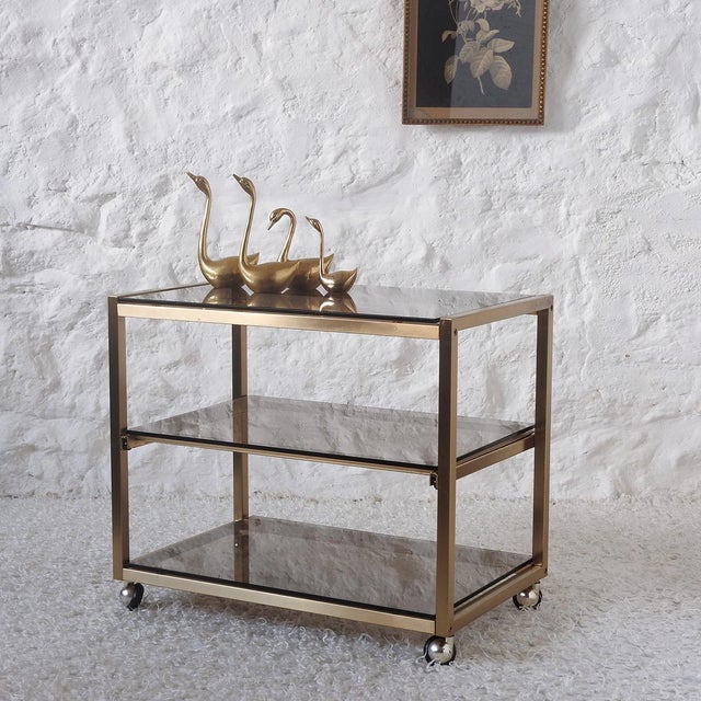 Gold-colored steel and smoked glass serving trolley with wheels for easy movement. The sliding central tray makes it ideal...
