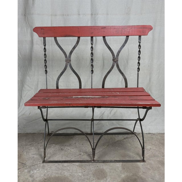 A mid-century French bistro style bench combining hand forged iron and painted wood. The frame features elegant arched...