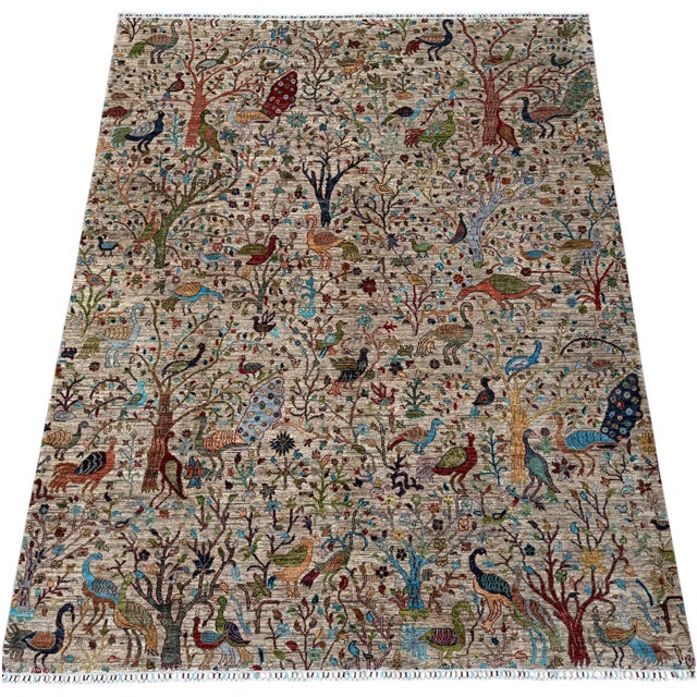 A hand-knotted Bird of Paradise rug, woven in Afghanistan on a soft oatmeal ground and filled edge to edge with a garden...