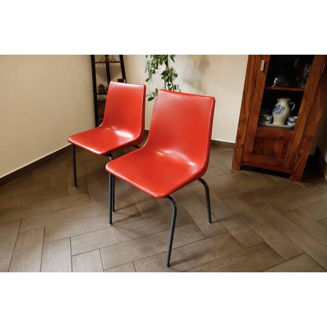 Pair of red plastic chairs from the 1980s featuring molded plastic seats and sturdy metal frames. Their minimalist and...