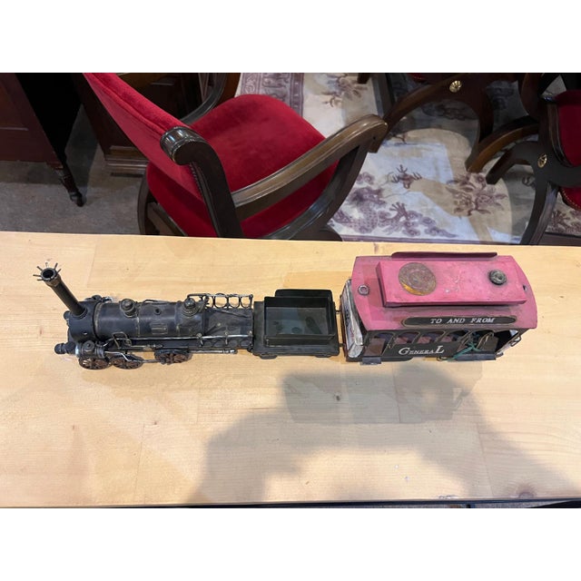 This detailed decorative metal train model featuring a classic steam locomotive, cargo car, and passenger coach with...