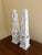 A pair of painted wood obelisks, rendered in a deliberately timeworn finish that evokes architectural fragments softened...