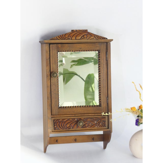 Small antique wooden wall cabinet with a rectangular mirror in the front door and a floral decorated drawer. The...