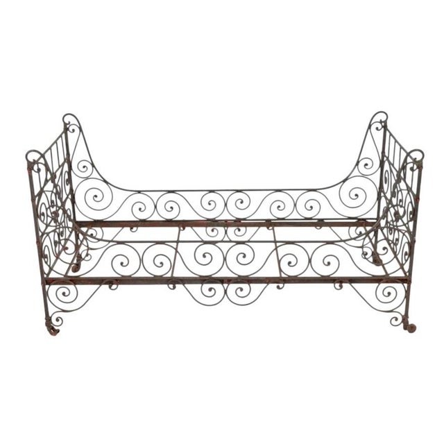 A French iron scrollwork daybed on metal casters. The iron frame is embellished with scrolled details throughout and...