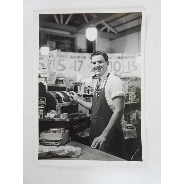 Vintage circa 1930's photograph of smiling grocery store check out man. Surrounded by advertising and products with chrome...